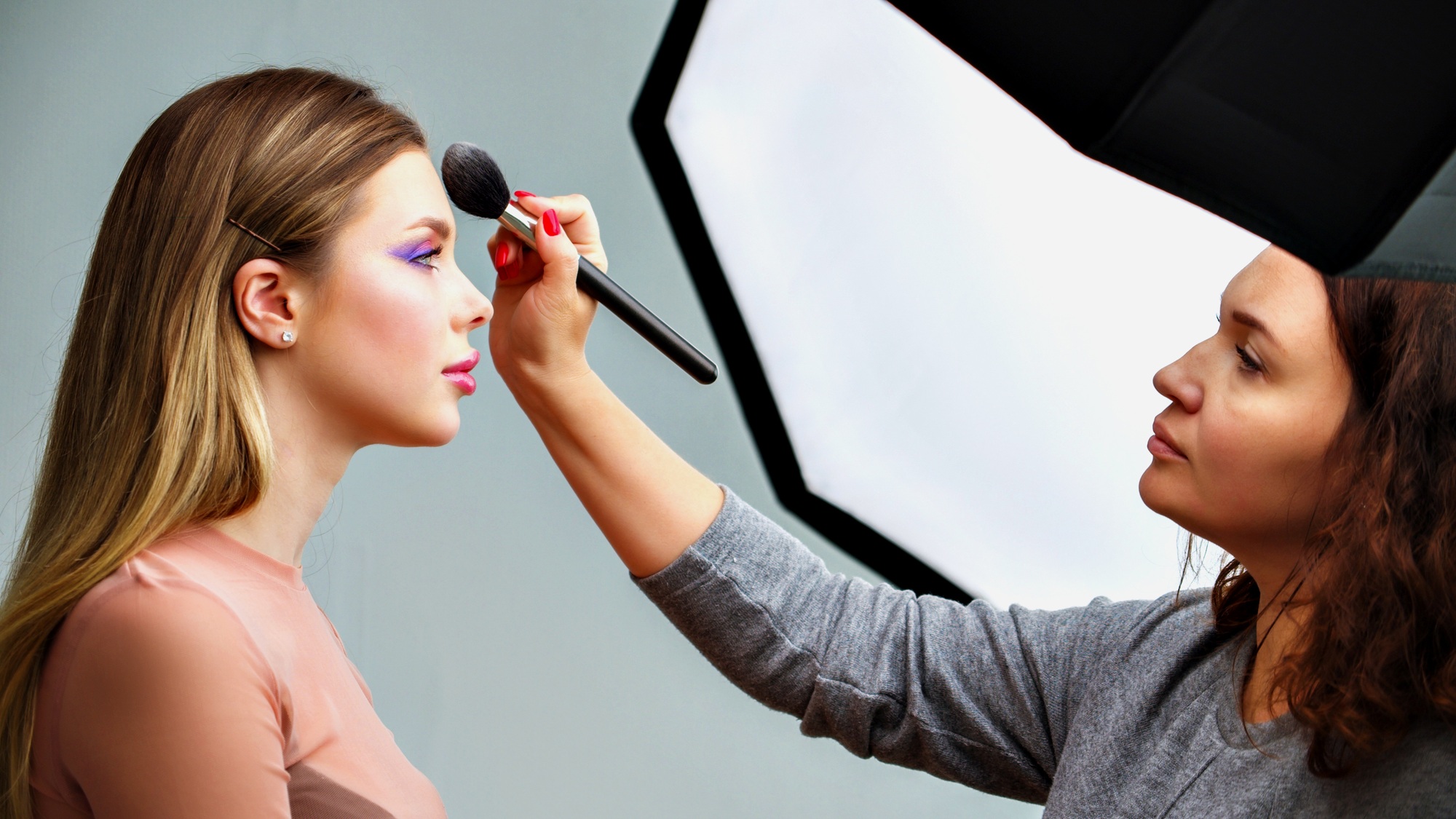 Backstage of the photo shoot: Make-up artist applies makeup on beautiful white model.