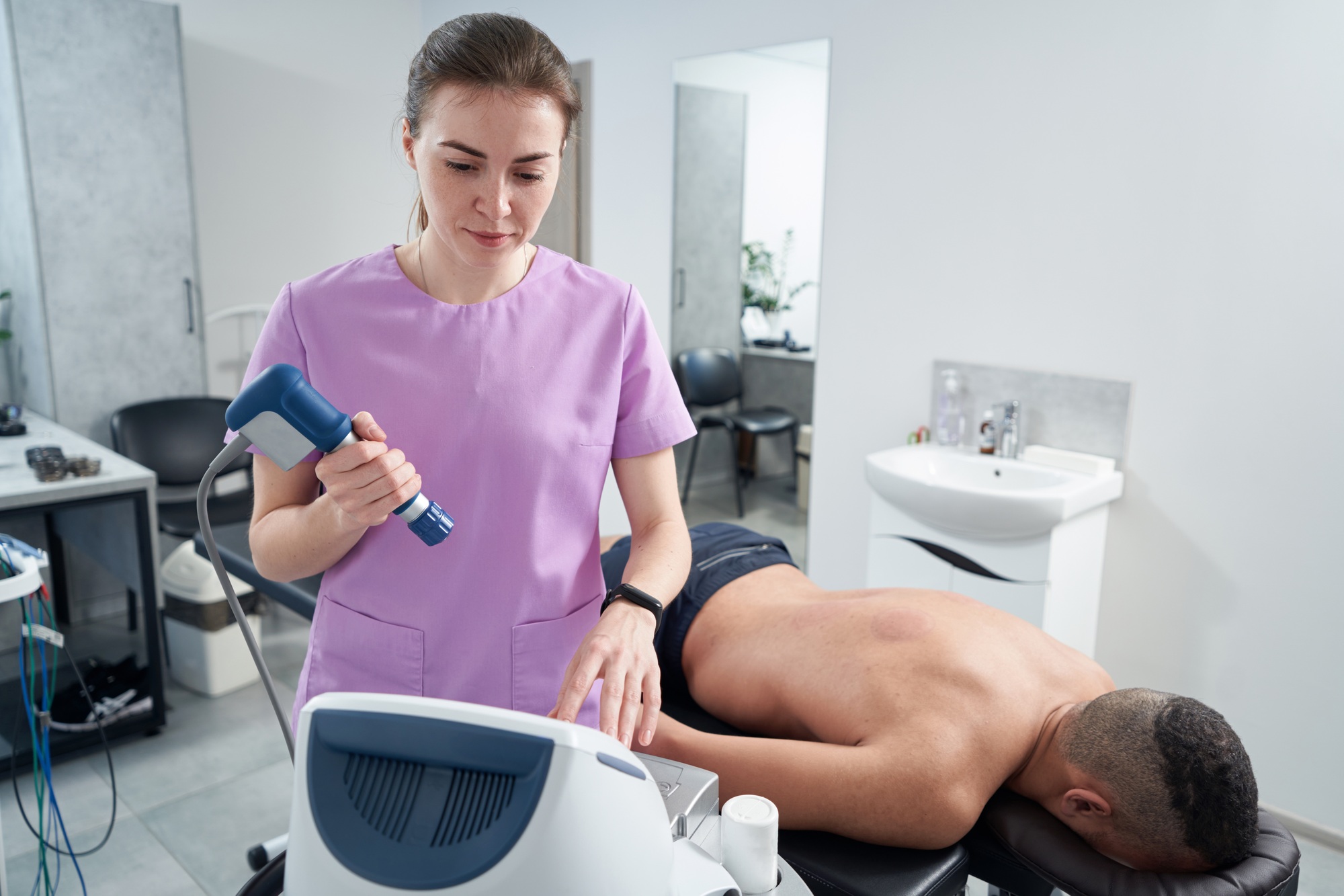 Doctor using extracorporeal shockwave therapy machine in clinic