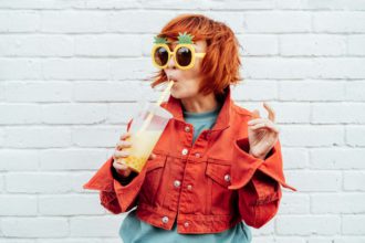 Hipster fashion young woman in bright clothes, funny pineapple glasses drinking tapioca bubble tea